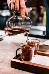 Male barista pouring expresso coffee into shot glass, making pour-over coffee with alternative...