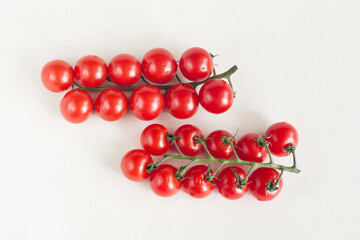 Two sprigs of cherry tomatoes lying parallel on a light background