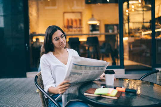 Focused Woman Looking Through Newspaper Outside Cafe