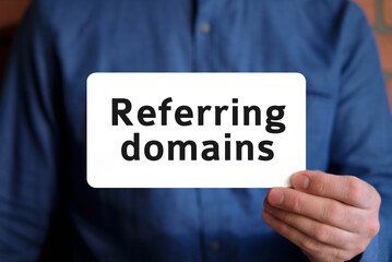 Referring domains - seo concept text on a white sign in the hand of a man in a blue shirt