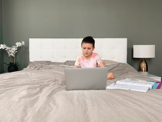 Caucasian boy child sitting in bed and learning online on laptop Internet. Virtual class lesson on video. Self isolation at home. Distant remote video education. A new normal school study for kids.