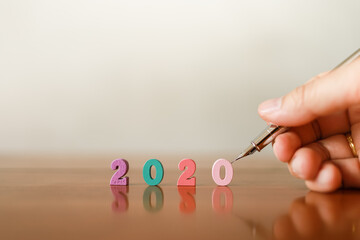 2020 New Year and Planning Concept. Closeup of man hand holding silver pen with colorful wooden number on wood table with copy space.