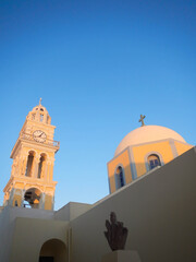 Greek Roman Catholic church. Сhurch dome matching the baroque yellow and gray coloring of the clock tower against sunset clear blue sky.