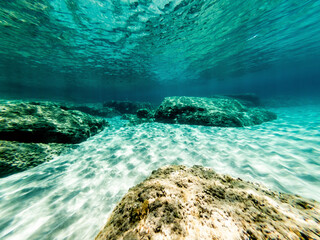 Underwater view of  rocks and white sand in Alghero shore