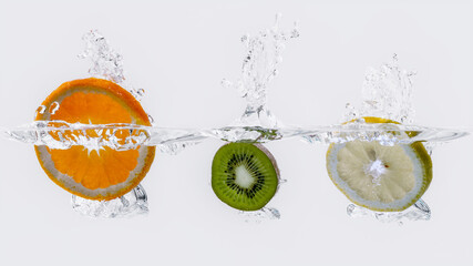 Eine Scheibe Kiwi, Zitrone und Orange fallen ins Wasser
