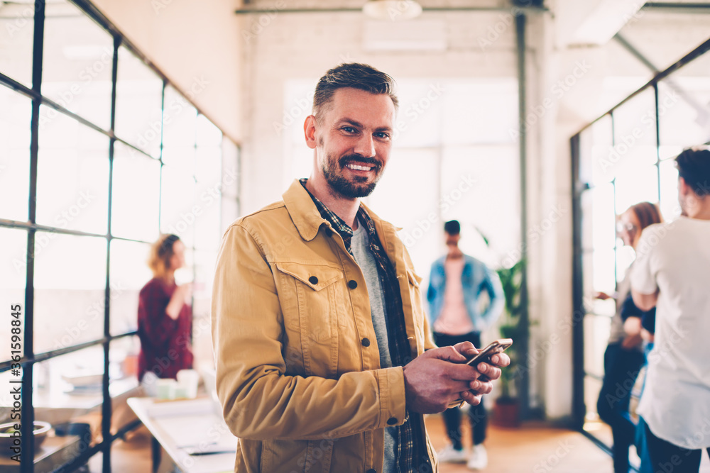 Poster half-length portrait of cheerful creative manager of designers team using mobile for sending message