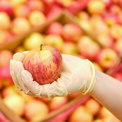 A hand in a protective glove holds a red apple near boxes in a store, close-up