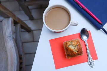 Close view of a coffee, banana muffin, tissue paper, pen, and notebook on white table 