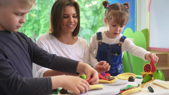 Caucasian girl and boy kid playing and learning at preschool with female teacher. Mother, daughter adn son playing cooking