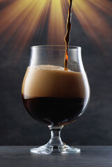 Stream of dark stout pours into a beer glass. Detail of dark beer with flowing foam head. 