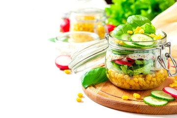Fresh vegetable salad in a mason jar close-up. Space for text. Salad of corn, radishes, cucumbers and lettuce in a glass jar on white background. Vegetarian food, healthy diet food.