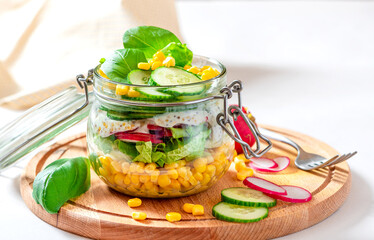 Fresh vegetable salad in a mason jar close-up. Salad of corn, radishes, cucumbers and lettuce in a glass jar. Vegetarian food, healthy diet food.