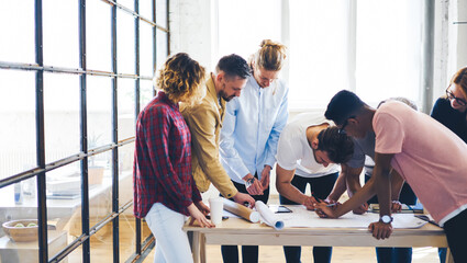 Students of university creating coursework project drawing blueprints during seminar with teacher giving advice about planning. graphic designers cooperating during working process in modern studio
