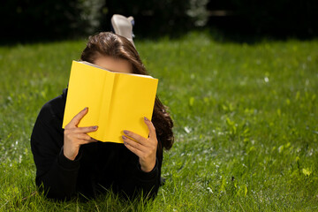 Attractive brunette girl with long hair dressed in black hoodie lying on grass of green lawn...