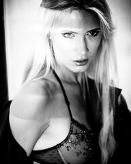 fashion and lingerie concept - beautiful blond lady portrait wearing sexy bra and panties in loft-style interior. Woman in underwear poses on a window in contrast light and shadows in monochrome.