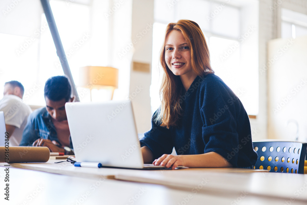 Poster portrait of charming young female student of university sitting in modern library while making homew