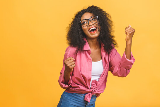 Happy winner! Young African American black woman isolated on yellow background giving a thumbs up gesture.