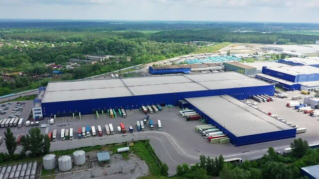 Aerial circling view of logistics center with warehouse, loading hub with many semi-trailers truck load.