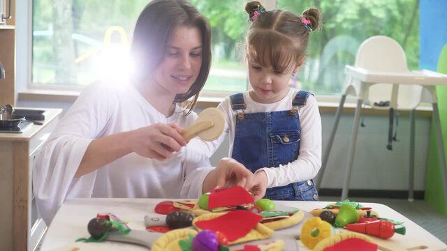 Caucasian girl and boy kid playing and learning at preschool with female teacher. Mother, daughter adn son playing cooking