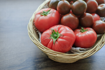 Tomatoes of different varieties in a wicker basket standing on a wooden background
