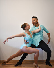 Professional Latino dance couple posing while dancing in light blue dresses