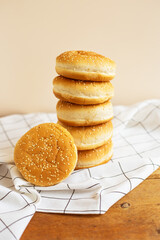Freshly baked magnificent buns for hamburgers lie durg on each other in the form of a tower on a wooden table with a white checkered napkin. Close-up.