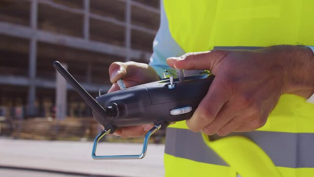 Professional drone operator in virtual reality helmet standing in front of construction site. Builder holding remote controller. Office building and crane background.