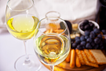 Two glasses of white wine and plate with assorted cheese, fruit and other snacks for party