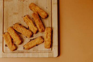 crispy fish sticks on a wooden cutting board and with orange background