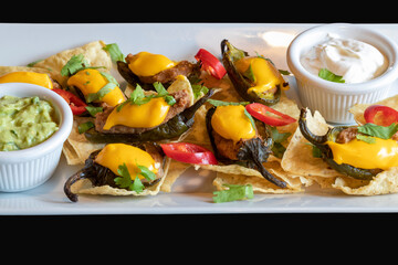 Roasted meat on chips decorated with peppers and cheese. The meat has avocado and garlic dip. The food is on a white plate isolated on a black background.