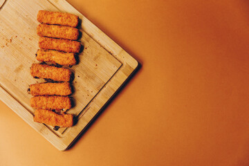 crispy fish sticks on a wooden cutting board and with orange background