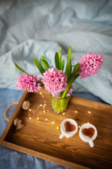 A bouquet of hyacinths, two cups of cappuccino stand on an old wooden tray.