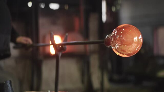 red hot glass on the end of a rod being turned by glass blowing artist - close up 