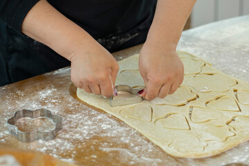 woman's hand slices sheet of dough with cookie mold in shape of heart and flowers for homemade cookies in kitchen сookery class. family traditions concept. Homemade baking lesson concept