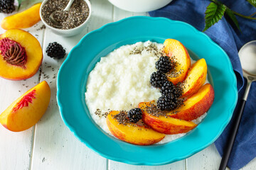 Healthy food for Breakfast, diet food concept. Rice porridge with chia, peach and blackberry in a bowl on a white wooden table.