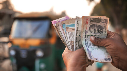 A man recounts Indian rupee money amid tuk tuk.