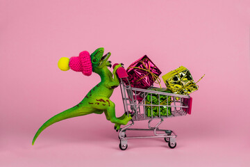 funny plastic toy dinosaur wearing tiny knitted hat and driving shopping trolley full of present...