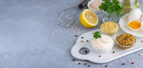 Cooked homemade mayonnaise in bowl with ingredients for cooking: eggs, olive oil, mustard, lemon on stone table