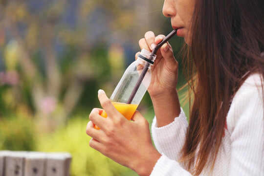 An Asian woman is drinking orange juice from a bottle..