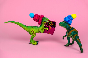 cute green toy dinosaur in knitted hat give present box to another dinosaur in hat, festive funny...