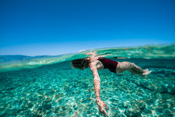 Carefree and relaxed, wide shot, young athletic woman effortlessly floats on her back in tropical...