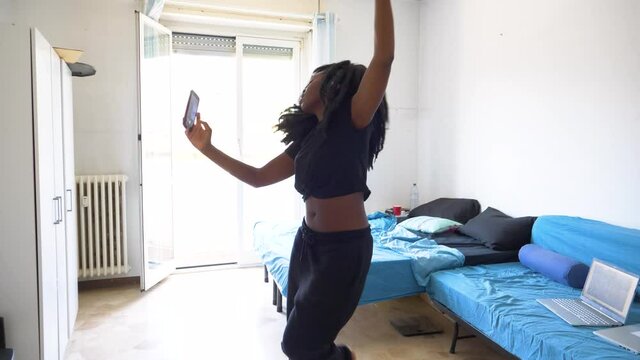 Slow motion shot of young woman dancing and using smartphone at home