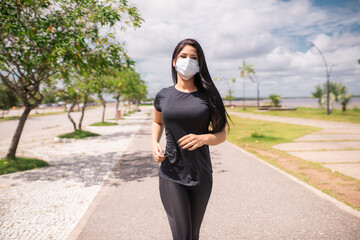 Linda mulher correndo rápido na calçada e ela usa uma máscara para proteção.
