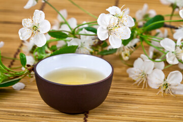Obraz na płótnie Canvas Green tea in a ceramic cup with branches of blossoming cherry tree on a bamboo background. Spring background.