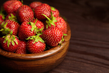 Strawberries in wooden bowl on brown table, closeup. Red ripe berries, fresh juicy strawberry on wooden background