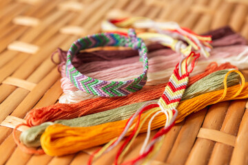 Woven bracelet made of bright cotton threads, colorful threads for embroidery and weaving on a rattan table. Selective focus. Hobbies, traditional art, jewelry in the style of boho, hippies. Handmade