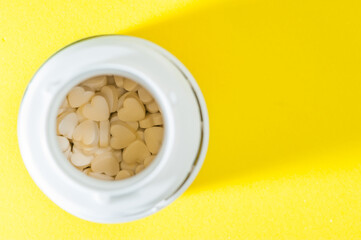 An open Jar with heart-shaped tablets, medications, dietary supplements on a yellow background.