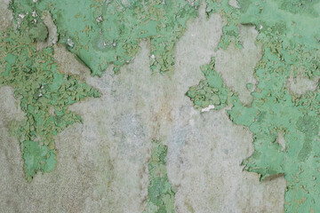 Green peeling paint on the wall. Old concrete wall with cracked flaking paint. Weathered rough painted surface with patterns of cracks and peeling. High resolution texture for background and design.