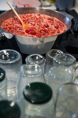 Cooking strawberry jam in a large bowl at home. Wooden spoon in a bowl with jam. Empty glass jars for jam.