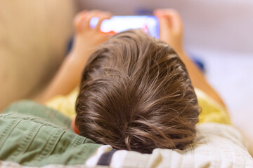 Adorable boy sitting on the sofa in the living room and playing with smartphone. Child learning how...